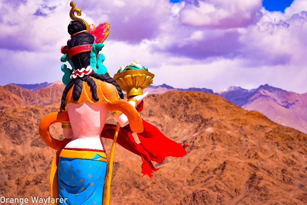 A Ladakhi Buddhist Statue stand against the barren Ladakhi mountains at Hemis Monastery, a day trip from Leh: Traveling in Ladakh